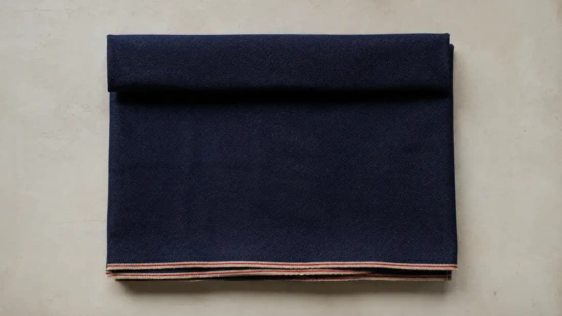A folded length of plain cloth photographed square from above, with the fold along the top and the two selvedge edges together at the bottom.