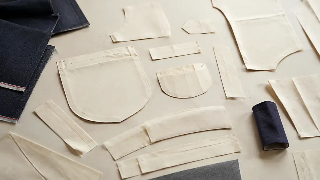 Cut paper pieces for a pocket, a facing, a cuff and a waistband laid in a group on a pale table.